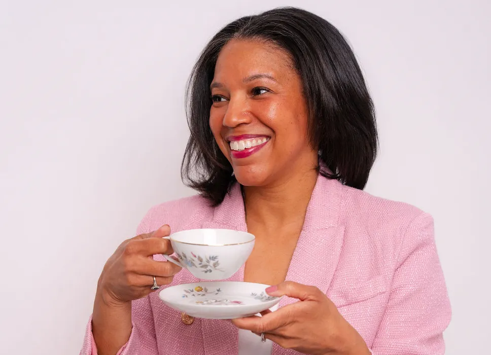 Cecelia Curtis smiling in a pink blazer while holding her grandmother Ada’s floral teacup and saucer